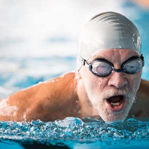 Senior man swimming in an indoor swimming pool. Senior man swimming in an indoor swimming pool. Active pensioner enjoying sport.